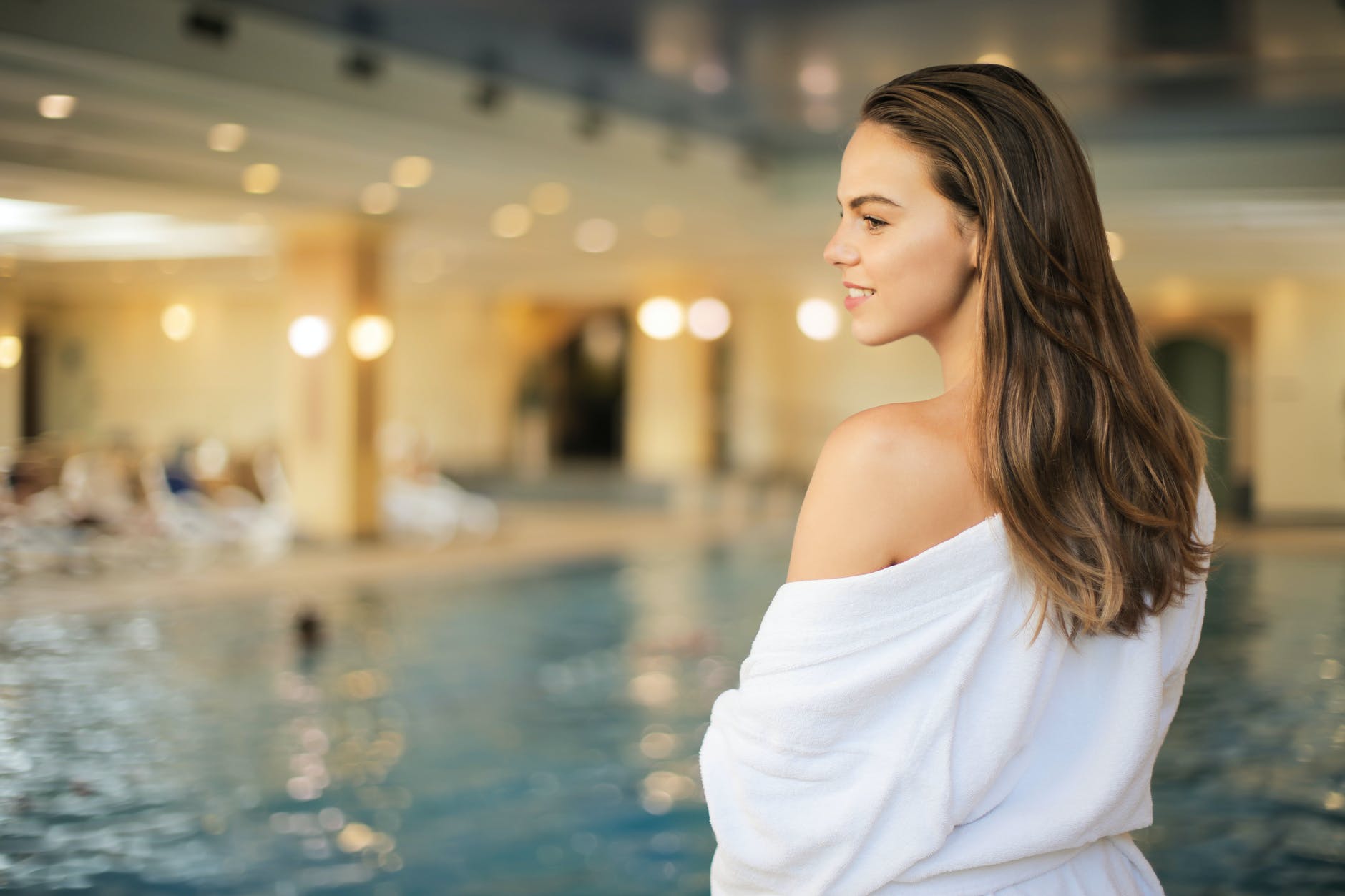 selective focus back view photo of smiling woman in white robe standing by poolside